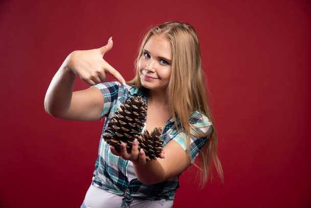Menina loira segura cone de carvalho na mão e parece positivo e alegre. Foto de alta qualidade - Foto, Imagem