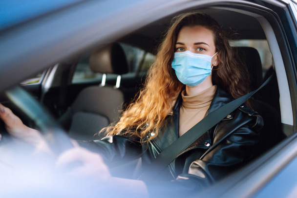 Young woman in protective medical mask driving a car. Covid-2019. Transport isolation. - Foto, Bild