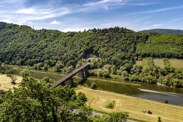 Stalowa konstrukcja kratownicy mostu kolejowego widziana z góry, w tle wzgórza porośnięte lasem i motorówką na rzece. - Zdjęcie, obraz