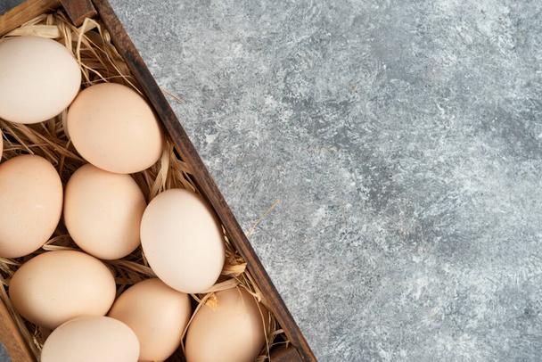 Wooden box of organic raw eggs on marble surface. High quality photo - Фото, зображення