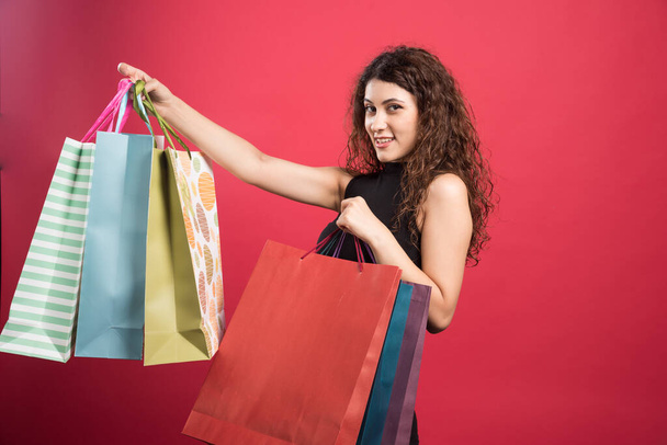 Žena ukazuje své nové nákupní oblečení na červeném pozadí. Kvalitní fotografie - Fotografie, Obrázek