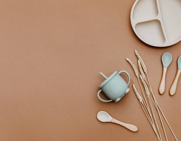 Set with bright baby dishware on table, silicone set on a trendy brown background, flat lay. Serving baby food. - 写真・画像