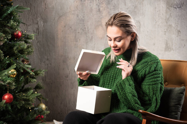 Молода жінка в зеленому теплому светрі схвильована подарунком. Високоякісна фотографія
 - Фото, зображення
