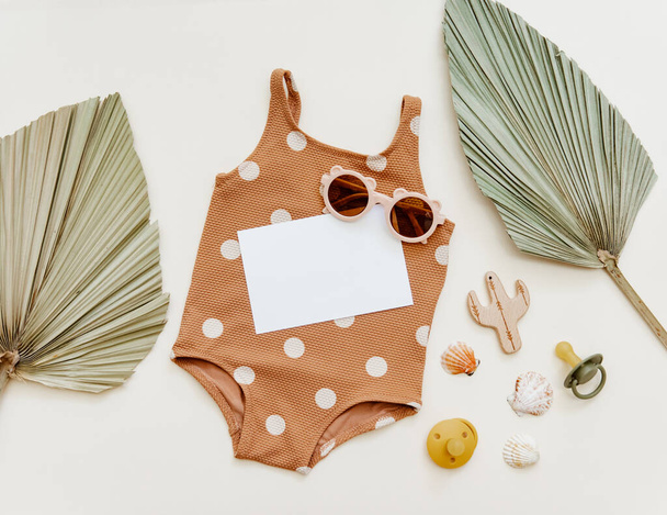 Retro swimsuit with baby accessories. Kids sunglasses, palm leaf and empty card. Summer Fashion newborn clothes. Holiday concept. Flat lay, top view - Φωτογραφία, εικόνα