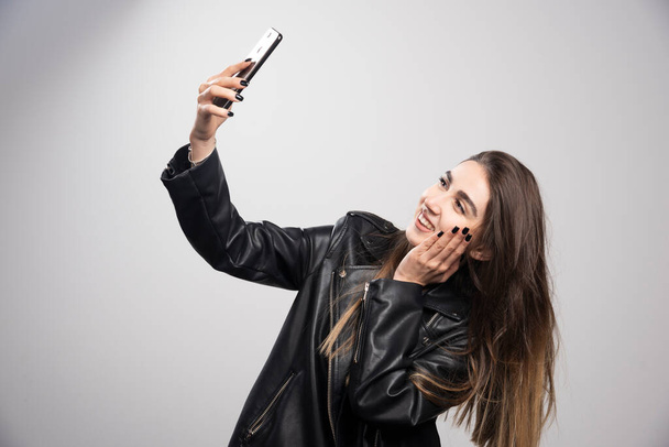 Young woman in leather jacket taking selfie with her cell phone . High quality photo - Photo, Image