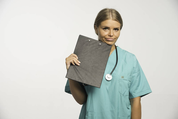 Блондинка-доктор в синей форме держит чековую книжку под подбородком. Высокое качество фото - Фото, изображение
