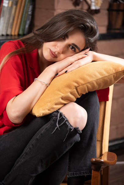 A young woman model in red blouse sitting and posing with a pillow . High quality photo - Фото, зображення