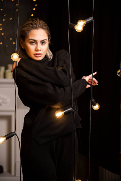 Retrato de una mujer encantadora mirando a la cámara en suéter oscuro de pie cerca de las lámparas. Foto de alta calidad - Foto, imagen