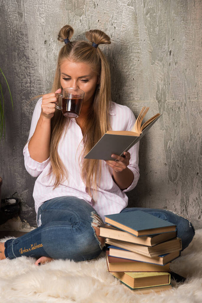 Женщина сидит на полу с книгой и пьет чашку чая на мраморном фоне  - Фото, изображение