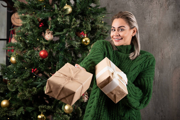Portrait of a girl dressed in green sweater giving a Christmas present. High quality photo - Photo, Image