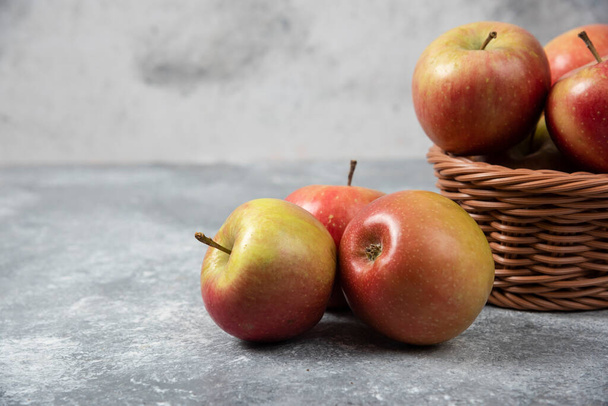 Wiklinowy kosz czerwonych soczystych jabłek na marmurowej powierzchni. Wysokiej jakości zdjęcie - Zdjęcie, obraz