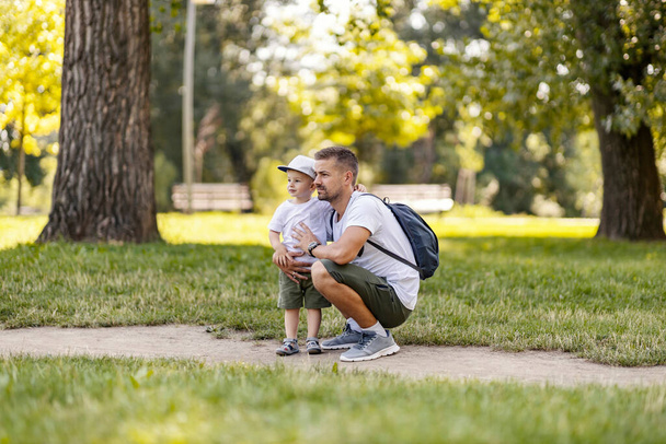 Holidays in the woods, family fun in the park, escape to nature and an active weekend. The father and son are dressed in the same clothes. Dad squats next to the boy and they look into the distance - Foto, imagen
