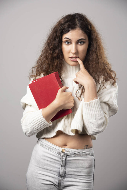 Mladá žena drží červenou knihu na šedé zdi. Kvalitní fotografie - Fotografie, Obrázek