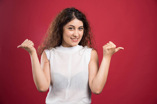 Smiling woman showing thumbs up on red background. High quality photo - Foto, afbeelding