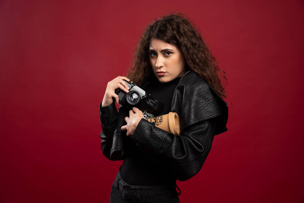 Young woman in all black outfit holding a cup and a camera. High quality photo - Foto, Imagem