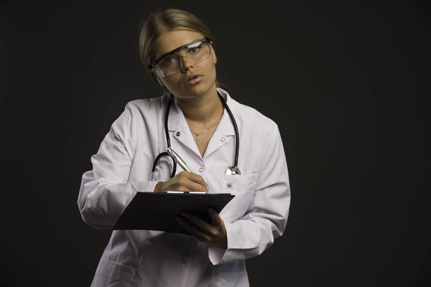 Blonde female doctor with a stethoscope wearing eyeglasses and writing a receipt . High quality photo - Photo, Image