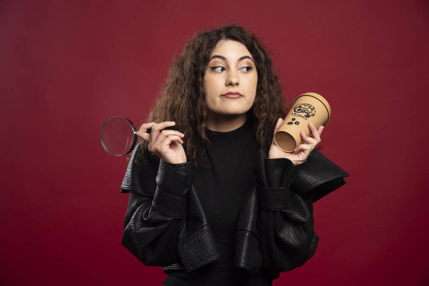Young woman in all black outfit holding a cup with loupe. High quality photo - Foto, immagini