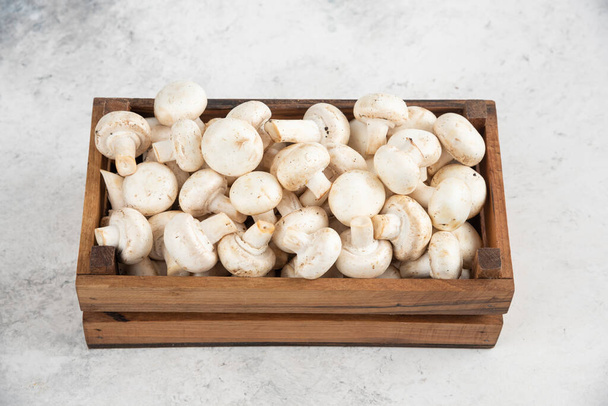 Cogumelos brancos dentro de uma bandeja de madeira em um fundo de mármore. Foto de alta qualidade - Foto, Imagem