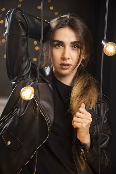 Portret van een prachtig jong model in zwart leren jasje poserend bij lampen. Hoge kwaliteit foto - Foto, afbeelding