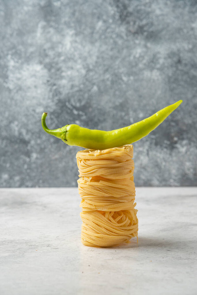Stack of raw pasta nests and green pepper on white table. High quality photo - Photo, Image