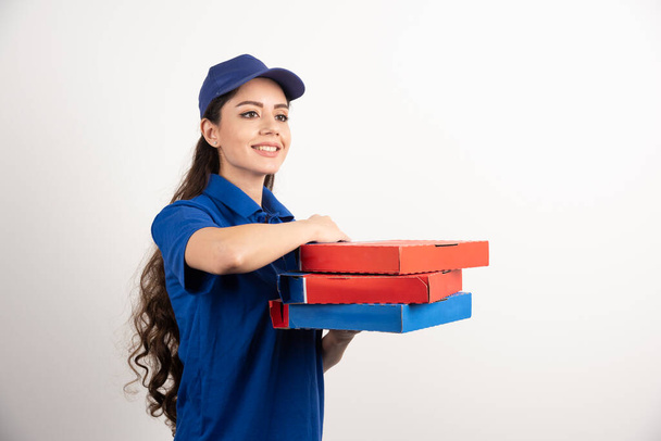 Menina de entrega sorridente feliz em uniforme azul com caixas de pizza takeaway sobre fundo branco. Foto de alta qualidade - Foto, Imagem