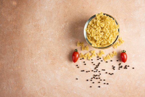 Raw pasta, pepper grains and fresh tomatoes on orange background. High quality photo - Foto, Imagen
