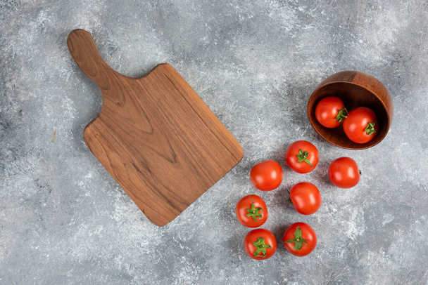 Tigela de madeira de tomates vermelhos com placa de corte sobre fundo de mármore. Foto de alta qualidade - Foto, Imagem
