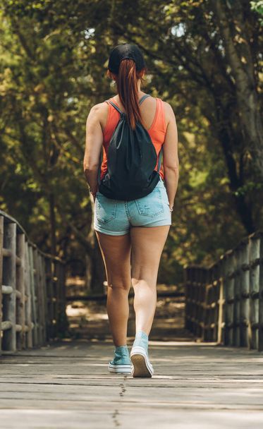 Rücken einer Frau in Sommerkleidung, die auf einem Holzweg geht - Foto, Bild