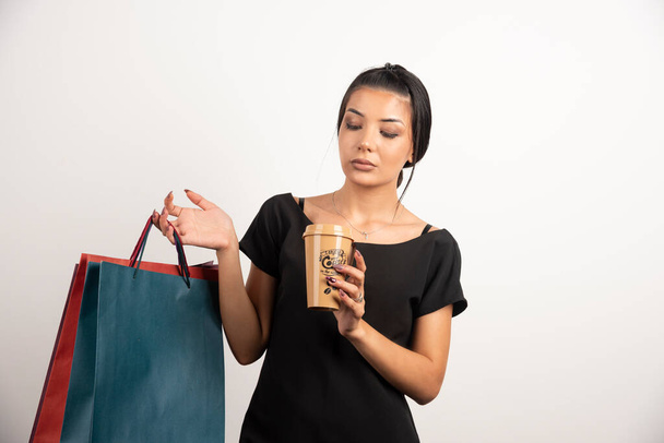 Müde Frau mit Kaffee und Einkaufstüten auf weißem Hintergrund. Hochwertiges Foto - Foto, Bild