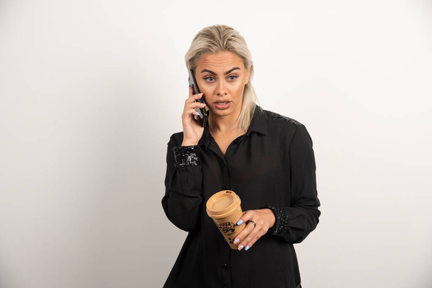 Ihmeellinen nainen puhuu matkapuhelimella ja pitelee kuppia kahvia. Laadukas kuva - Valokuva, kuva