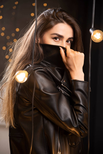 Retrato de una hermosa modelo joven en chaqueta de cuero negro posando cerca de lámparas. Foto de alta calidad - Foto, Imagen