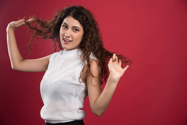 Pretty woman touching her curly dark hair on red background. High quality photo - Photo, Image