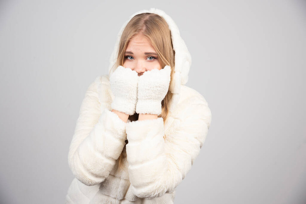 Happy woman in fur coat covering her face on gray background. High quality photo - Fotoğraf, Görsel