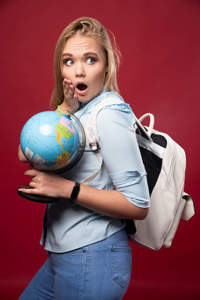Студентка блондинка держит глобус и выглядит удивленной. Высокое качество фото - Фото, изображение