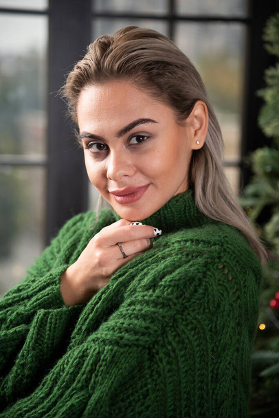 Pretty woman wearing green sweater near Christmas tree. High quality photo - Photo, Image