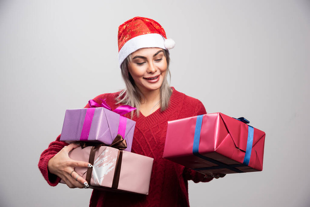 Schöne Frau mit Weihnachtsmütze beim Betrachten von Weihnachtsgeschenken. Hochwertiges Foto - Foto, Bild