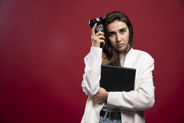 Business woman with a cup holding a notebook on a red background. High quality photo - Φωτογραφία, εικόνα