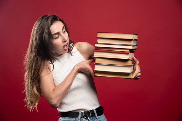 Young girl student holds a stack of books on a red background. High quality photo - Fotoğraf, Görsel