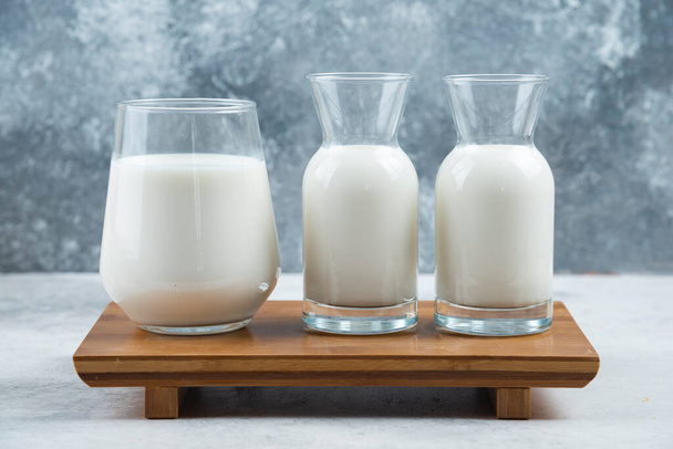 Szklana szklanka mleka i dwa szklanki mleka na drewnianym biurku. Wysokiej jakości zdjęcie - Zdjęcie, obraz