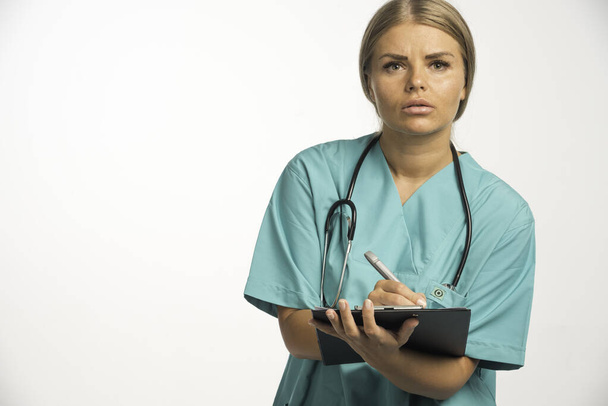 Médica loira de uniforme azul com estetoscópio no pescoço escrevendo um recibo. Foto de alta qualidade - Foto, Imagem