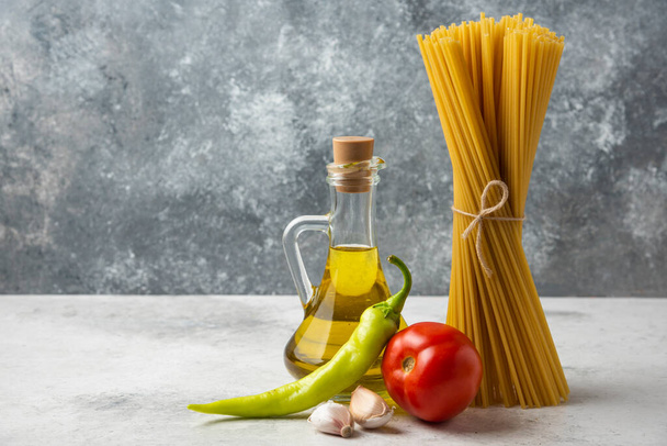 Száraz spagetti, egy üveg olívaolaj és zöldség a fehér asztalon. Kiváló minőségű fénykép - Fotó, kép
