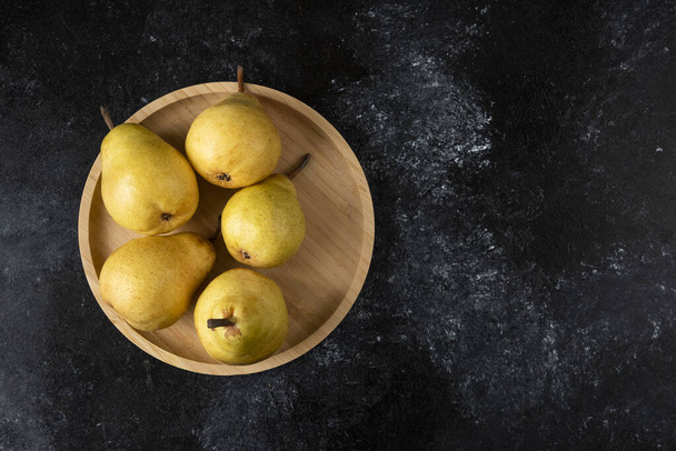 Wooden plate of tasty yellow pears on black surface. High quality photo - Foto, Imagem