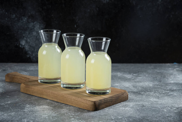 Trois cruches en verre de jus de citron frais sur une planche en bois - Photo, image