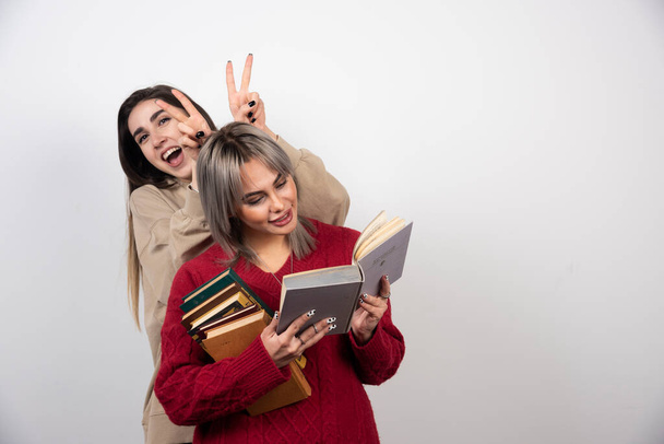 One girl doing bunny ears another girl who reading a book. High quality photo - Photo, image