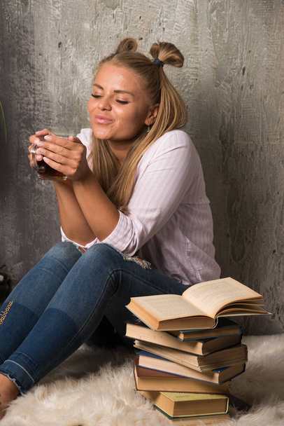 Smiling woman sitting on floor with tea and book on marble background - Valokuva, kuva