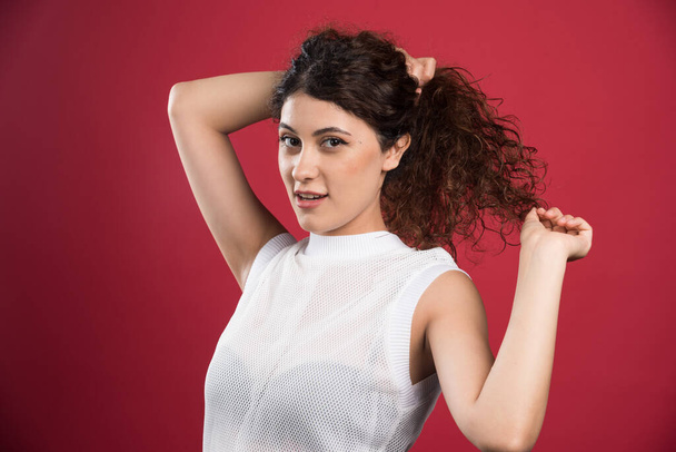 Pretty woman touching her curly dark hair on red background. High quality photo - Photo, Image