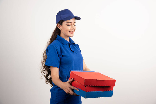 Ευτυχισμένο χαμογελαστό κορίτσι παράδοση σε μπλε στολή με κουτιά πίτσα takeaway πάνω από λευκό φόντο. Υψηλής ποιότητας φωτογραφία - Φωτογραφία, εικόνα