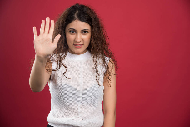 Woman with curly hair doing stop sing on red background . High quality photo - 写真・画像