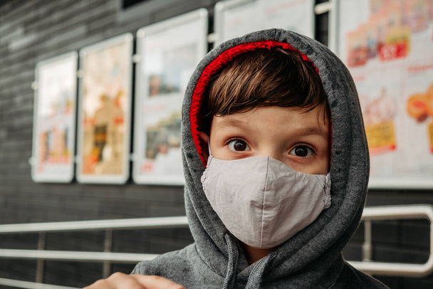 Chłopiec w masce ochronnej wchodzi do supermarketu. Ochrona dziecka przed covid-19 koronawirusem w supermarkecie. - Zdjęcie, obraz