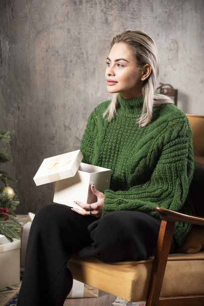 Nuori nainen vihreässä puserossa istuu ja poseeraa lahjapakkauksen kanssa. Laadukas kuva - Valokuva, kuva